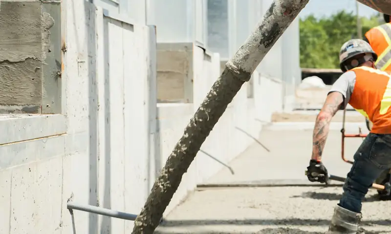 Pump hose placing concrete beside a commercial building while the crew rakes and screeds