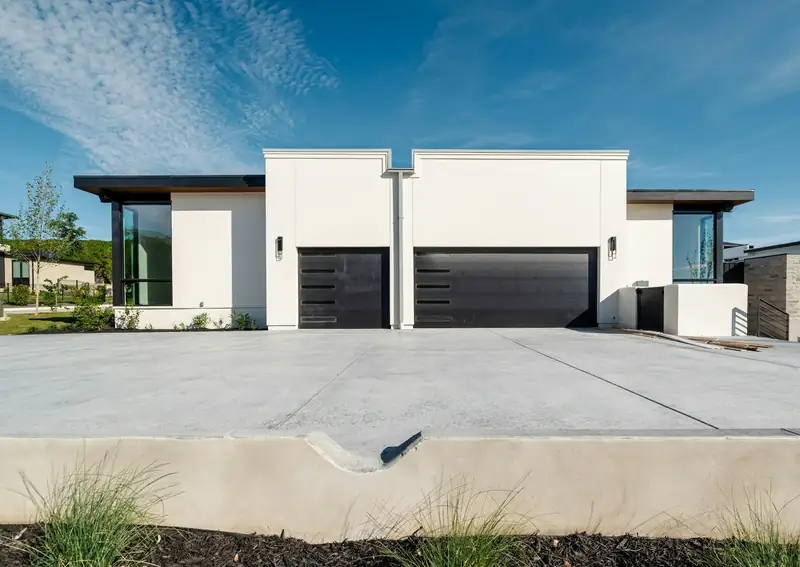 Wide new light-gray concrete driveway with diagonal control joints in front of a white three-garage home