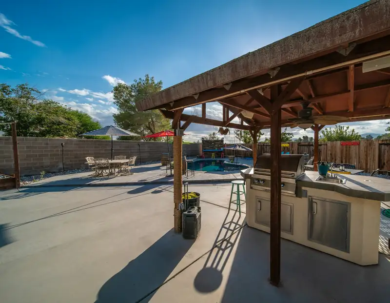 Broom-finished backyard concrete patio with control joints under a wood patio cover and outdoor kitchen