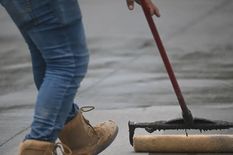 Long-handled roller spreading a coat across a concrete slab surface