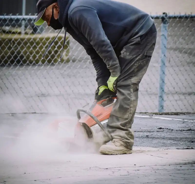 Worker saw-cutting a cracked slab so the damaged section can be removed and repoured