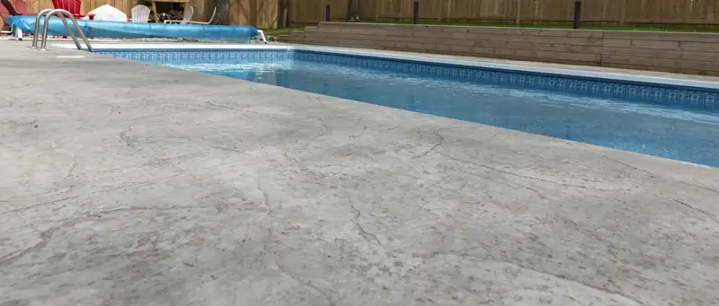 Gray stamped concrete pool deck with a slate texture running along an in-ground pool