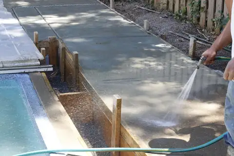 Hose washing the surface paste off a fresh pool-deck pour to expose the aggregate